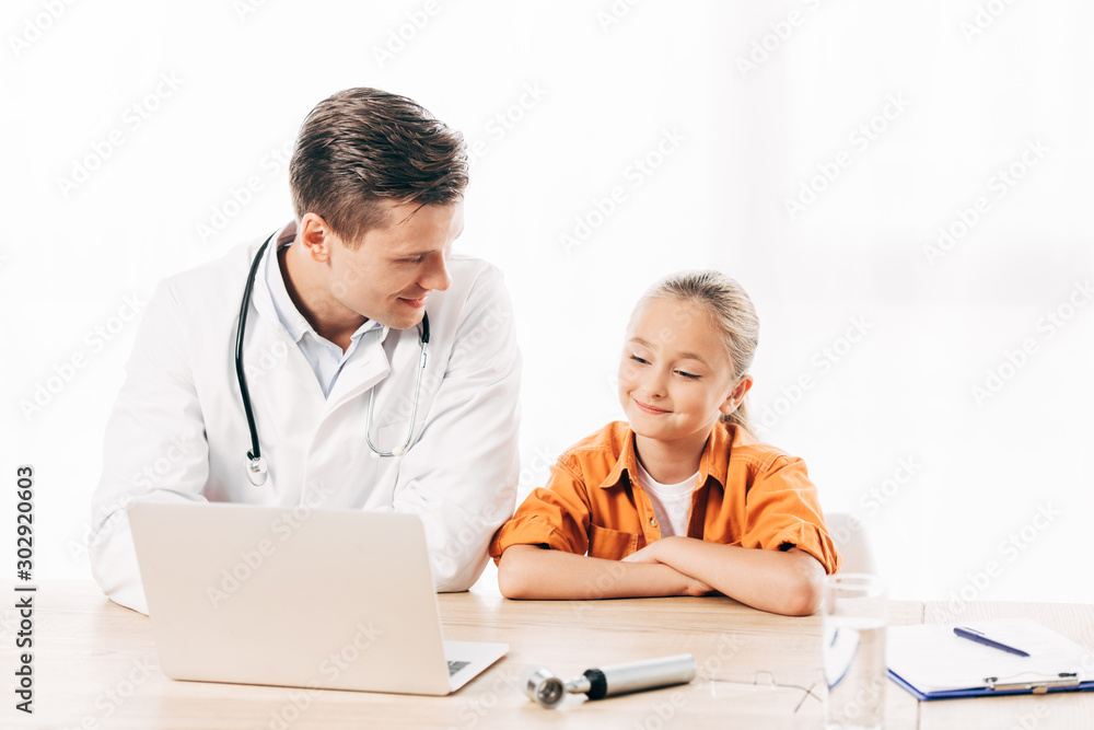 smiling pediatrist in white coat and child using laptop in clinic smiling pediatrist in white coat and child using laptop in clinic