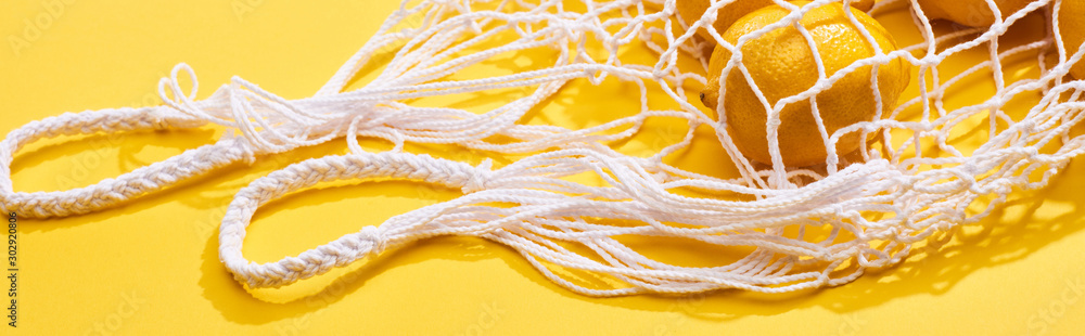 fresh ripe whole lemons in eco string bag on yellow background