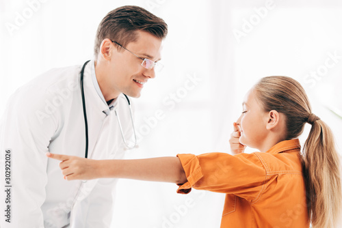 smiling pediatrist in white coat and child touching nose in clinic