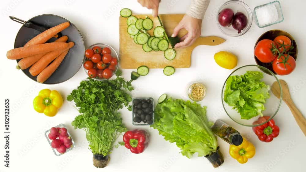 healthy eating, vegetarian food and cooking concept - young woman with kitchen knife chopping cucumber on wooden cutting board and adding to salad at home healthy eating, vegetarian food and cooking concept - young woman with kitchen knife chopping cucumber on wooden cutting board and adding to salad at home