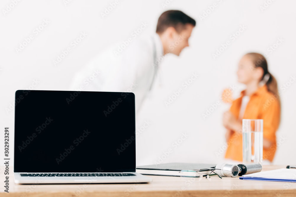 selective focus of pediatrist and child and laptop with blank screen on foreground selective focus of pediatrist and child and laptop with blank screen on foreground