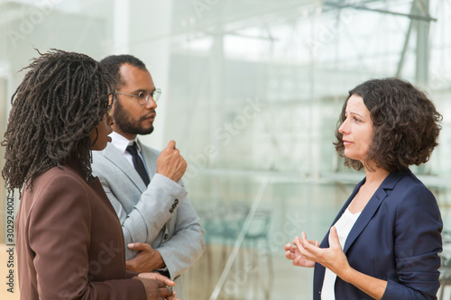 Focused mux raced colleagues discussing project. Business man and women standing at outdoor glass wall, talking to each other. Cooperation concept photo