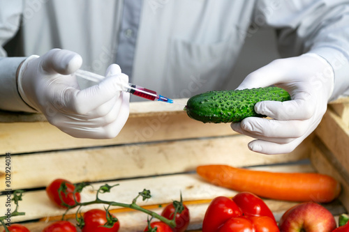 A man injects chemicals into a cucumber, fertilizers and chemicals with a syringe to increase the shelf life of vegetables. Chemical processing of vegetables, injection with chemicals.