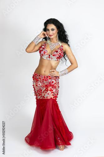 Brunette in a beautiful long red dress to perform belly dance white background. Girl in a red dress for oriental dancing.