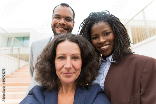 Happy successful business team taking selfie outside. Self portrait of business man and women standing near office building, smiling. Unity or teamwork concept