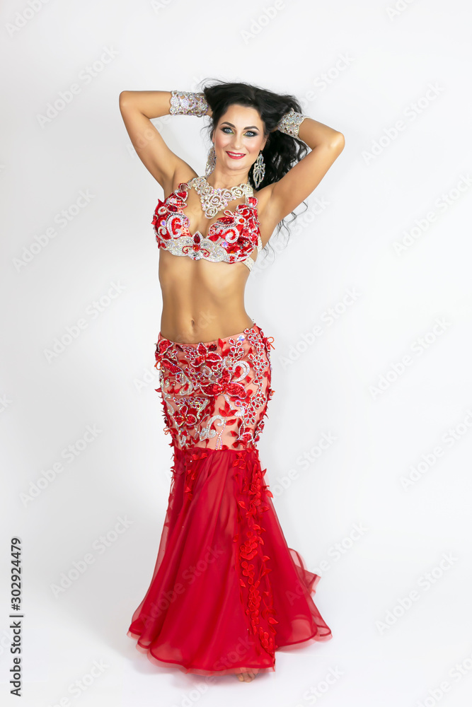 Girl in a red dress for oriental dancing. Brunette in a beautiful long red dress to perform belly dance on white background.