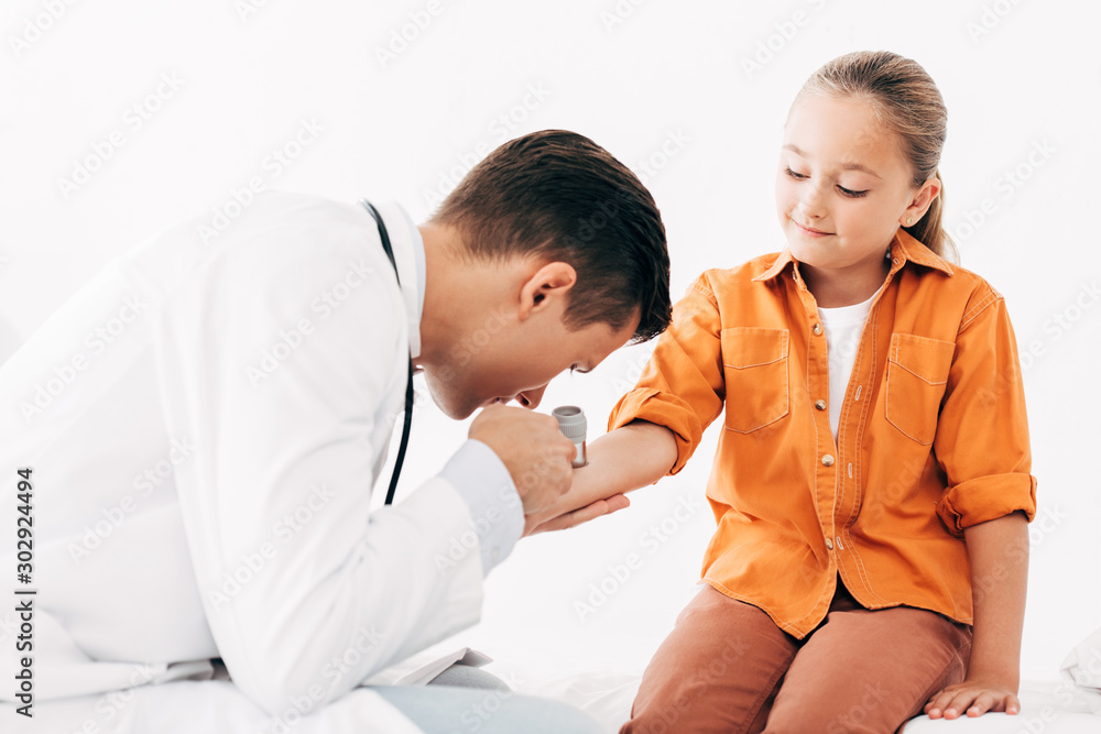 pediatrist in white coat examining child with dermascope pediatrist in white coat examining child with dermascope