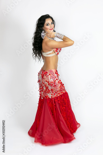 Girl in a red dress for oriental dancing. Brunette in beautiful long red dress to perform belly dance on a white background.