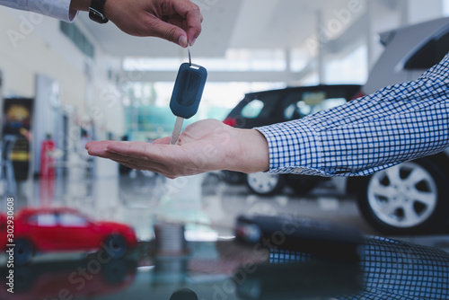 Male car salesman is going to give a new car key to an Asian business customer and sign a car dealer contract to buy a new car loan, trade money or investment.