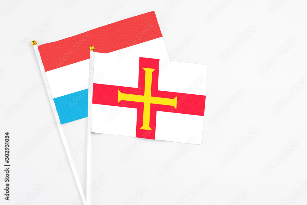 Guernsey and Luxembourg stick flags on white background. High quality fabric, miniature national flag. Peaceful global concept.White floor for copy space.