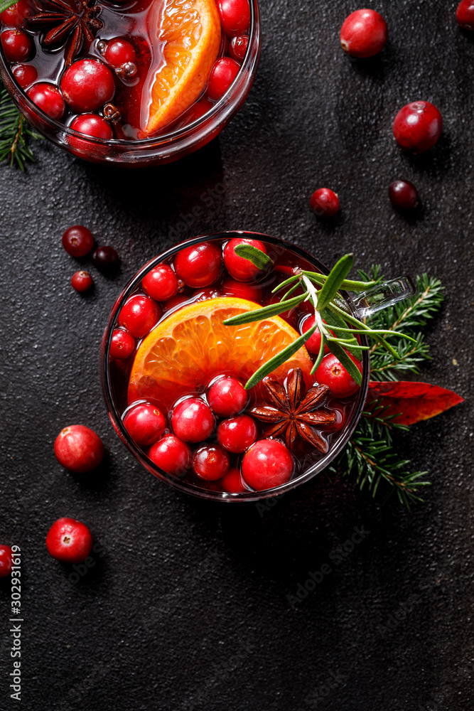 Christmas mulled wine with addition of cranberries, citrus fruits, aromatic spices and herbs in glass cups on a black background, top view. Delicious traditional christmas hot drink Christmas mulled wine with addition of cranberries, citrus fruits, aromatic spices and herbs in glass cups on a black background, top view. Delicious traditional christmas hot drink