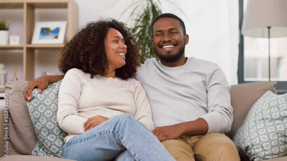 love, valentines day and relationships concept - happy african american couple sitting on sofa at home and kissing love, valentines day and relationships concept - happy african american couple sitting on sofa at home and kissing