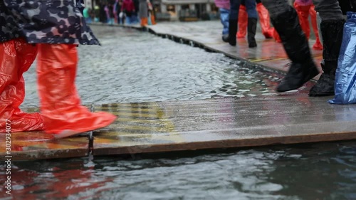 People with plastic gaiters or with boots on the walkway during the flood in Venice in Italy
