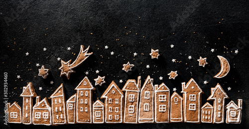 Christmas background, gingerbread cookies houses and gingerbread stars on a black background. Christmas gingerbread town