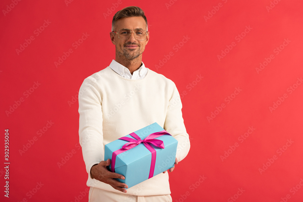 positive man in glasses holding gift box isolated on red positive man in glasses holding gift box isolated on red