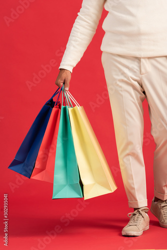 cropped view of man holding colorful shopping bags isolated on red