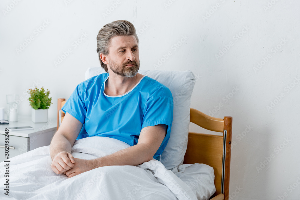 handsome patient in medical gown looking away in hospital handsome patient in medical gown looking away in hospital