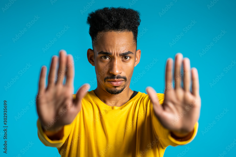 No, never, handsome african american man disliking and rejecting gesture by stop sign. Portrait of young successful confident guy isolated on blue No, never, handsome african american man disliking and rejecting gesture by stop sign. Portrait of young successful confident guy isolated on blue