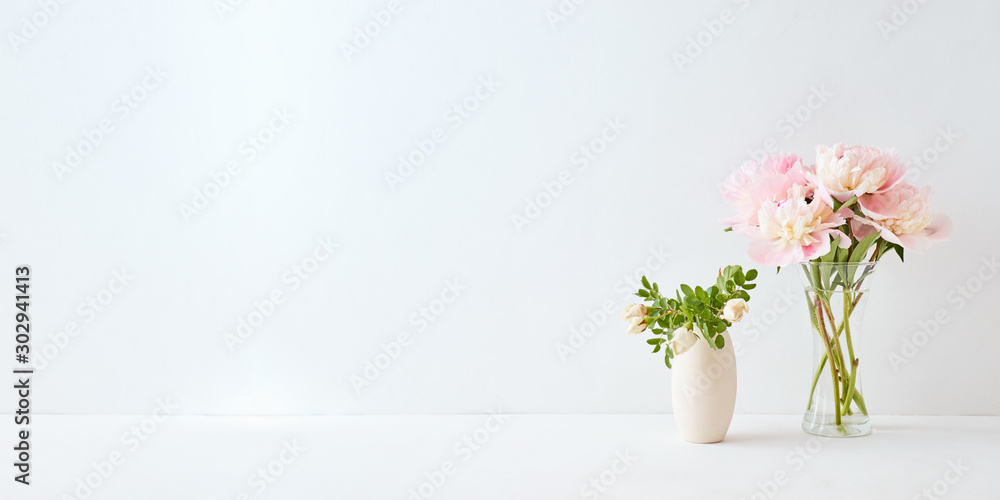 Home interior with decor elements. Pink peonies in a vase and white flowers on a white background