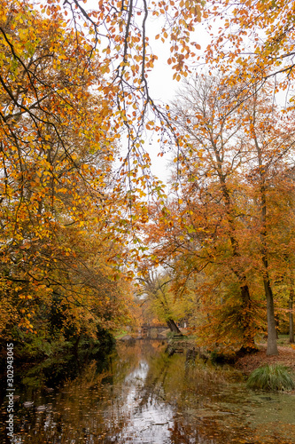Fototapeta Naklejka Na Ścianę i Meble -  Trees in autumn colors reflected in the water of a canal with an old bridge with three arches in the background