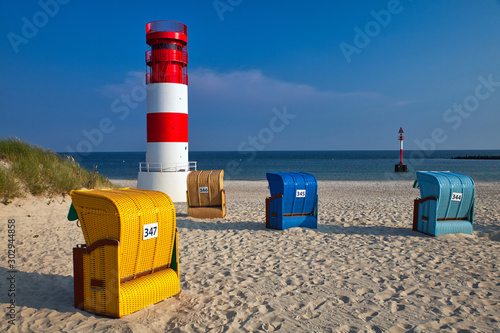 colorful beach chairs and red and white lighthouse on düne with empty beach