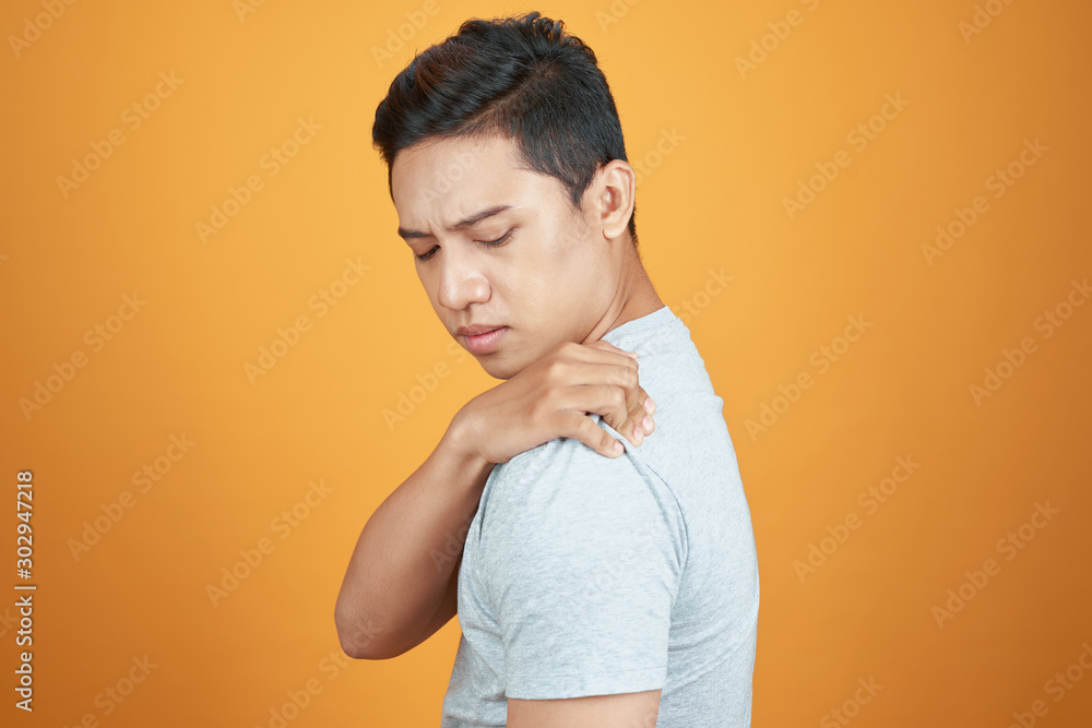 Young Asian man in casual with shoulder pain. Isolated on orange background Young Asian man in casual with shoulder pain. Isolated on orange background