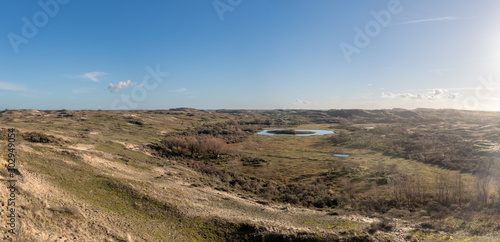 Panoramic view from a high dune top on a valley with a dune lake and the contours of a village on the horizon