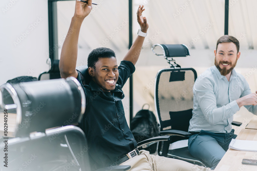 Obraz premium Portrait of happy african american student holding hands up and rejoicing completing task during private lesson with tutor.Two positive colleagues in formal wear celebrating victory of common project