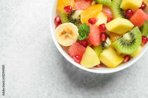 Bowl with homemade fresh fruit salad: mango, grapefruit, pomegranate, kiwi, banana on a light background top view copy space.