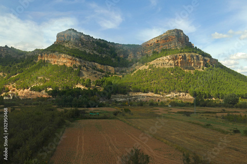 Panorama view on empty farmers fields in front of green overgrown flat-top mount / table top mountain in the south of Spain north of the Sierra de Andújar at beautiful weather with blue sky