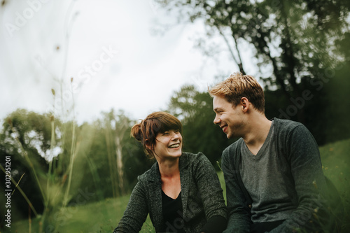 young heterosexual couple sitting in the grass smiling © kay fochtmann