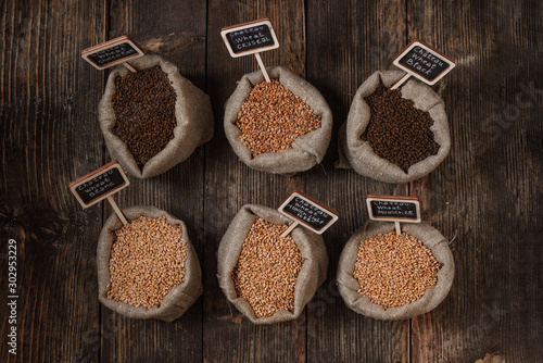 Grain of wheat, rye and barley in small burlap sacks on a wooden background. Name of the variety of grains on a wooden plate frame. Rustic, farm concept. Copy space. Top view