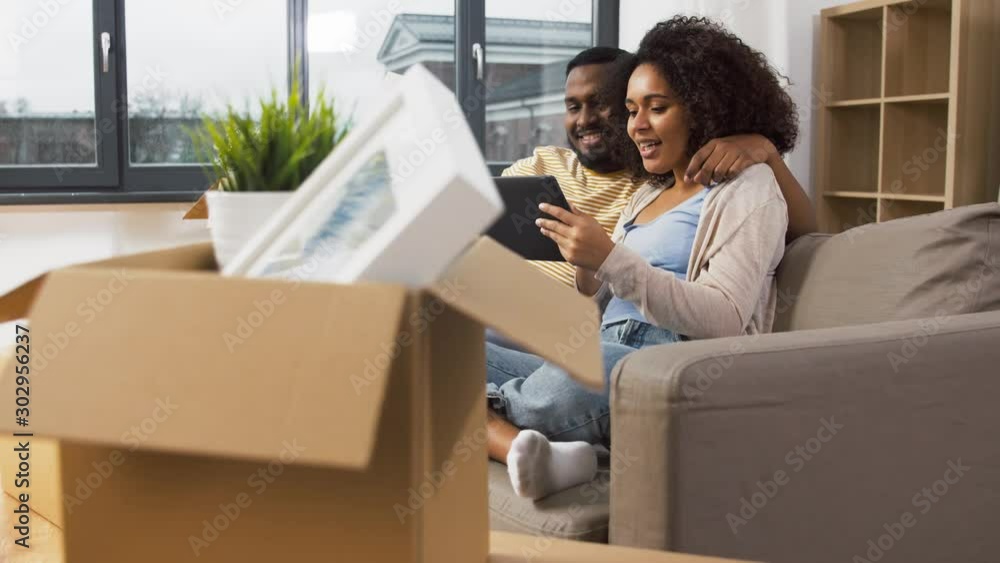 mortgage, people and real estate concept - happy african american couple with tablet pc computer sitting on sofa at new home mortgage, people and real estate concept - happy african american couple with tablet pc computer sitting on sofa at new home