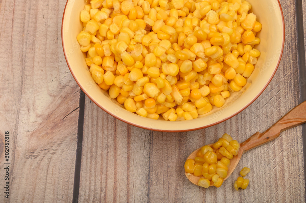 Sweet corn kernels in a plate and on a wooden spoon on a wooden table. Fitness diet. Healthy diet. For a sweet treat. Sweet corn kernels in a plate and on a wooden spoon on a wooden table. Fitness diet. Healthy diet. For a sweet treat.