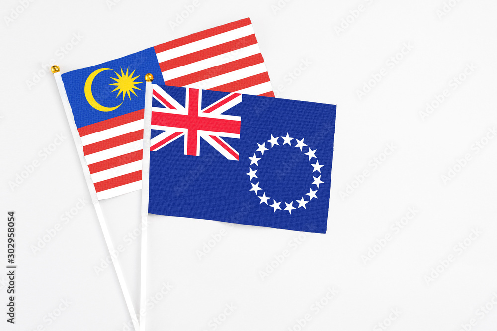 Fototapeta premium Cook Islands and Malaysia stick flags on white background. High quality fabric, miniature national flag. Peaceful global concept.White floor for copy space.