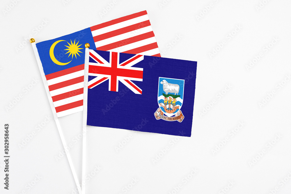 Fototapeta premium Falkland Islands and Malaysia stick flags on white background. High quality fabric, miniature national flag. Peaceful global concept.White floor for copy space.