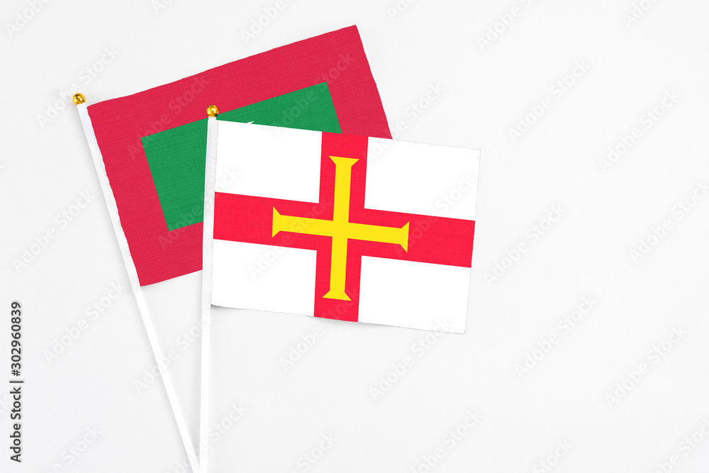 Guernsey and Maldives stick flags on white background. High quality fabric, miniature national flag. Peaceful global concept.White floor for copy space.