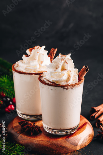 Traditional Christmas drink Eggnog with whipped cream and cinnamon on dark stone background. photo