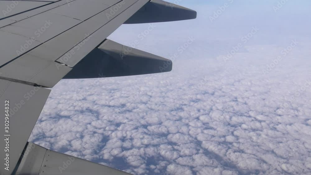 Under the wing of an airplane. Flying above the white clouds at blue sky background - view from an aircraft window. Under the wing of an airplane. Flying above the white clouds at blue sky background - view from an aircraft window.