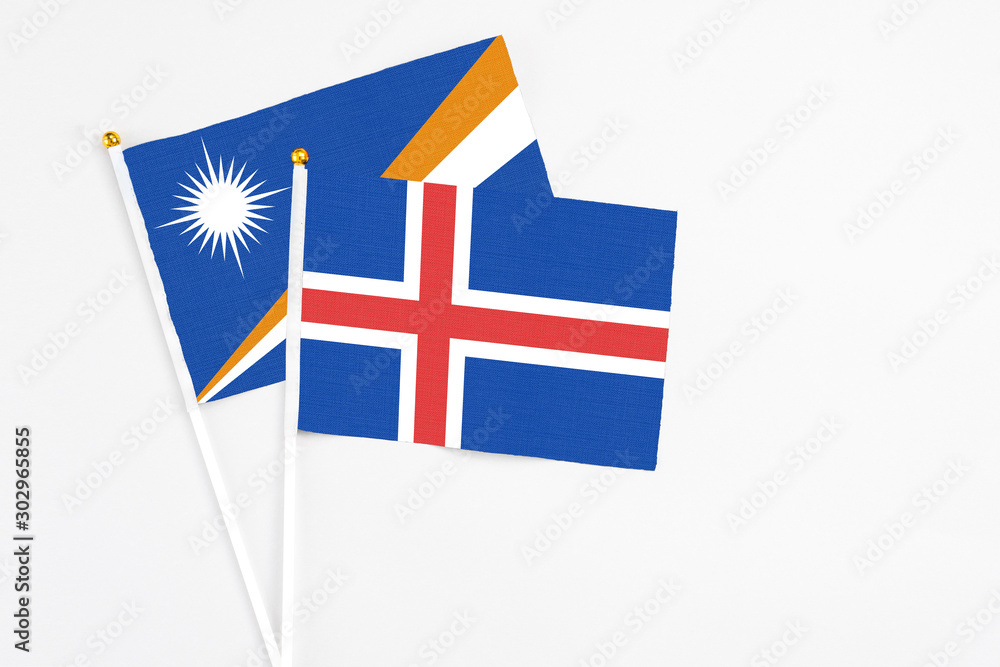 Fototapeta premium Iceland and Marshall Islands stick flags on white background. High quality fabric, miniature national flag. Peaceful global concept.White floor for copy space.