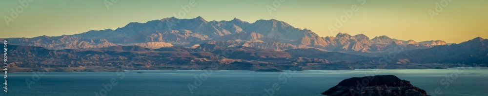 Morning light over Lake Meade with an island in the foreground and a mountain in that background.