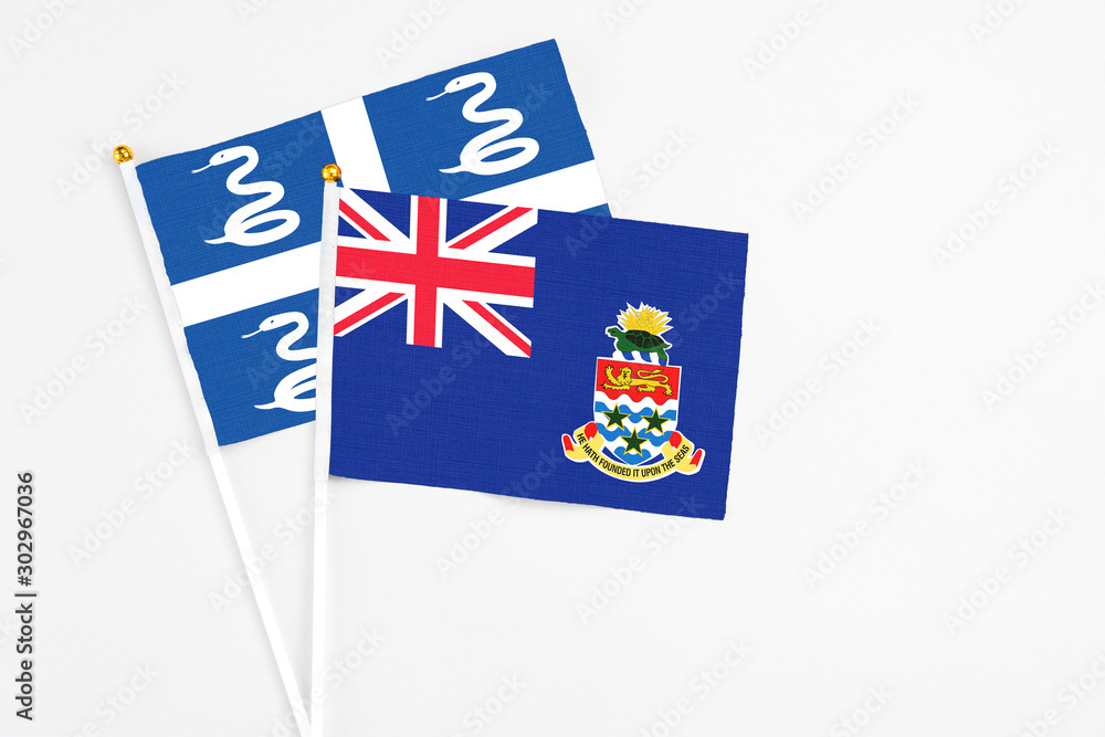 Fototapeta premium Cayman Islands and Martinique stick flags on white background. High quality fabric, miniature national flag. Peaceful global concept.White floor for copy space.