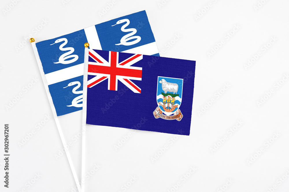 Fototapeta premium Falkland Islands and Martinique stick flags on white background. High quality fabric, miniature national flag. Peaceful global concept.White floor for copy space.