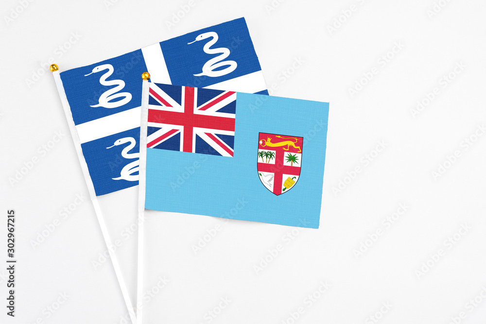 Fototapeta premium Fiji and Martinique stick flags on white background. High quality fabric, miniature national flag. Peaceful global concept.White floor for copy space.