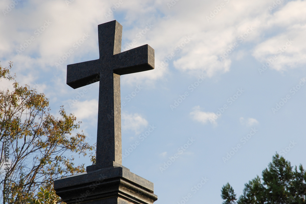 Black granite stone cross against blue sky at cemetery