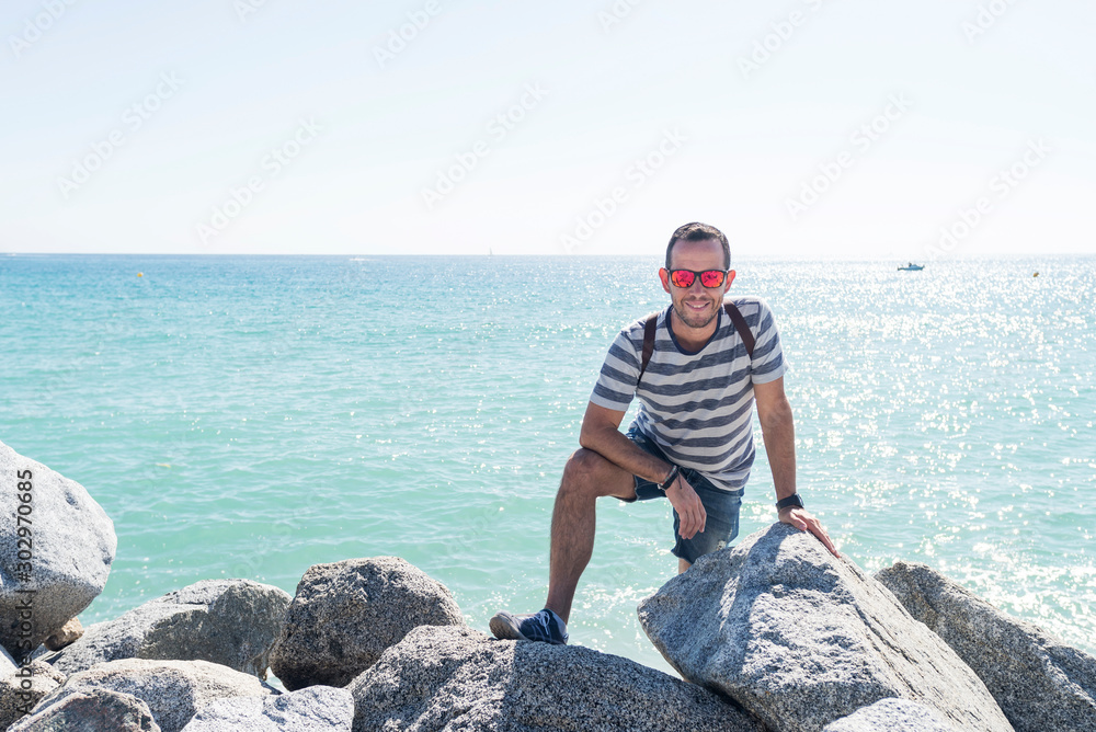 Portrait of a young man with sunglasses on seashore while looking to camera