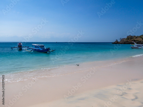 A view on a bay on Pink Beach  Lombok Indonesia. A few colourful boats anchored to the shore. The water has many shades of blue. The heavenly beach is surrounded by small hills. Paradise beach.