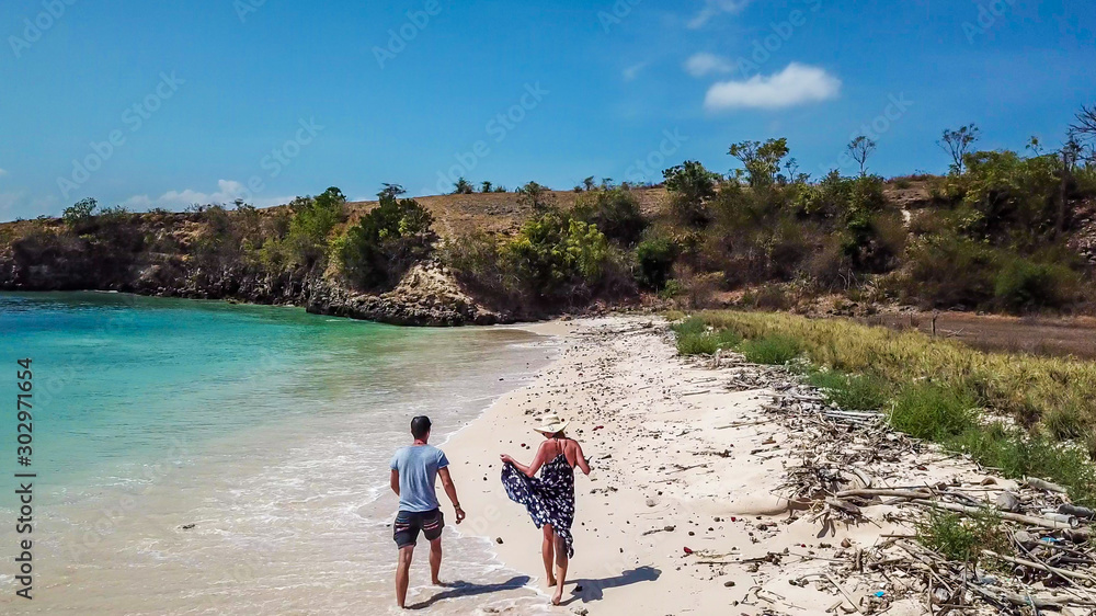 A couple walking on the Pink Beach in Lombok, holding hands. This place is a hidden gem, not spoiled by tourists. Solitude and calm feelings, waves gently spreading on the beach.