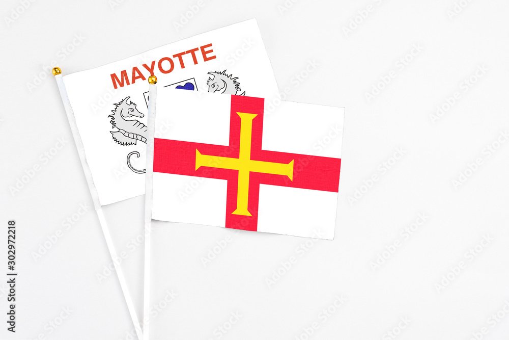 Guernsey and Mayotte stick flags on white background. High quality fabric, miniature national flag. Peaceful global concept.White floor for copy space.
