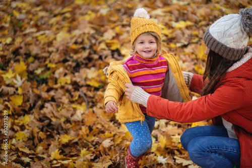 mom puts on her little daughter's jacket in the autumn forest